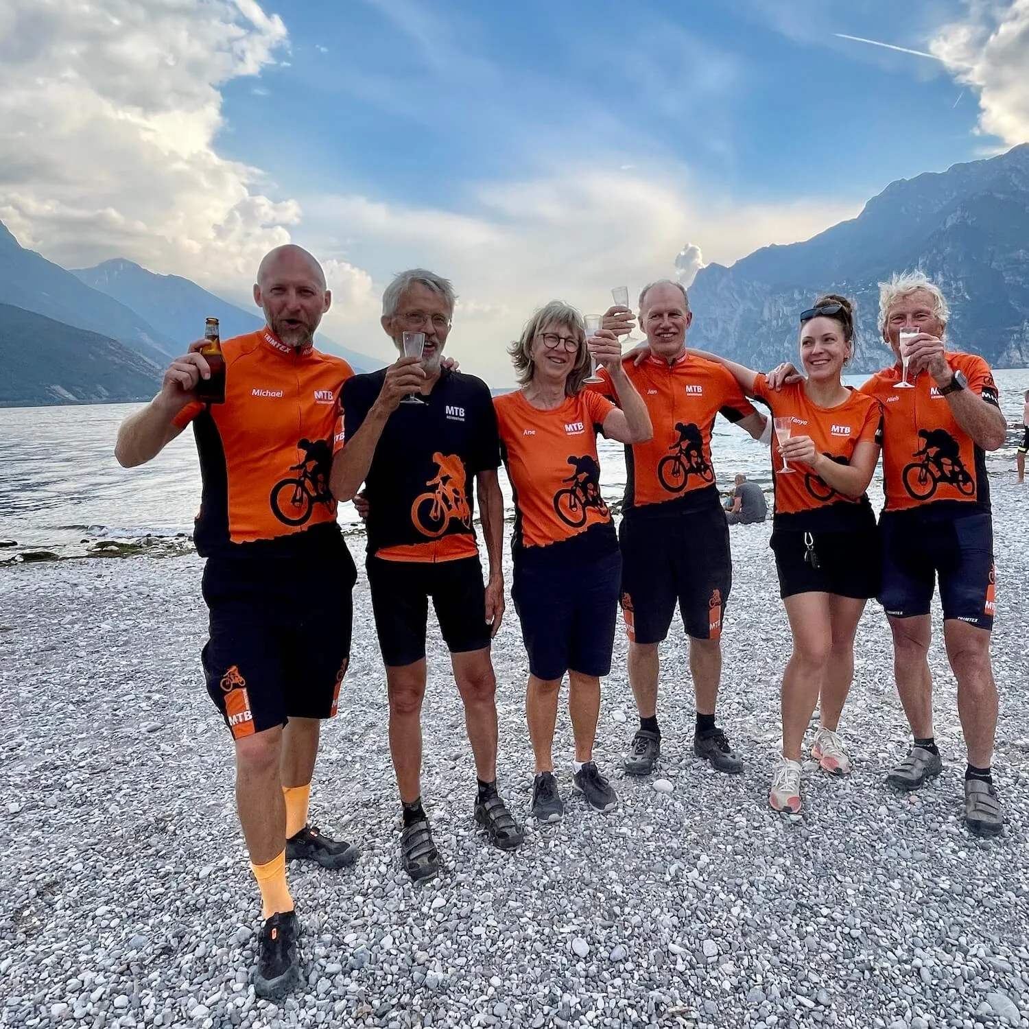 En liten Gravel Adventure-gruppe skåler ved bredden av Gardasjøen etter en Trans Alp-graveltur