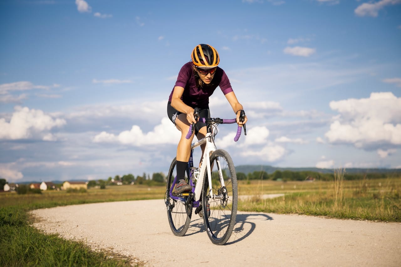 En gravelcyklist kører alene ad en grusvej gennem åbent landskab i solskin