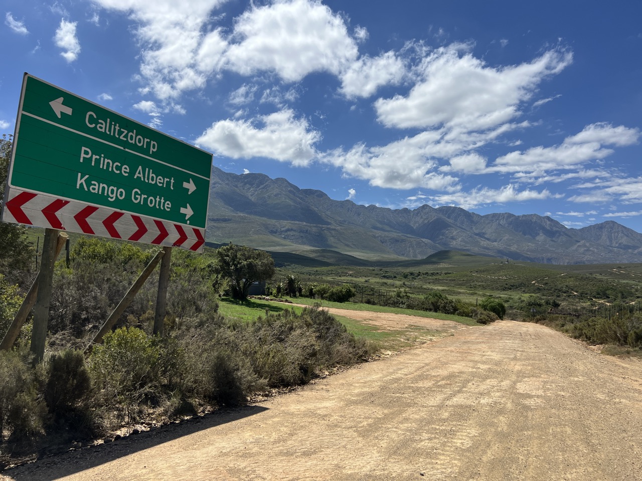 Et vejskilt der peger mod Calitzdorp, Prince Albert og Kango-hulerne, med Swartberg-bjergene i baggrunden